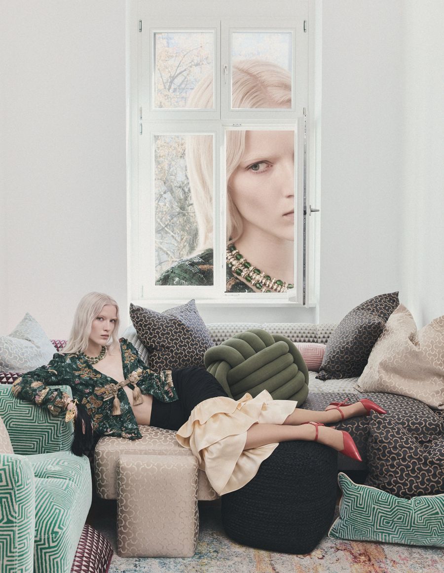 Editorial with a blonde model on a sofa and a second face in the window